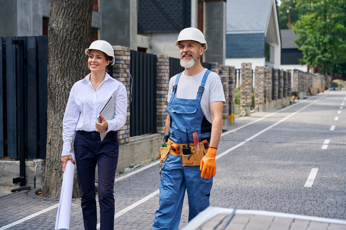 Designer with rolled plans and a contractor walking along a paver driveway