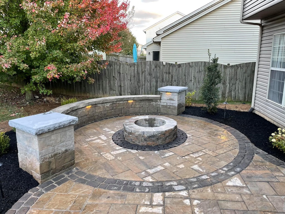 Circular paver patio with a stone fire pit, curved seat wall and two capped pillars