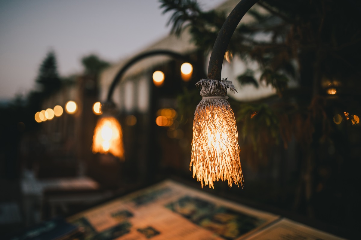 Close-up of a woven pendant light glowing over an outdoor patio table at dusk