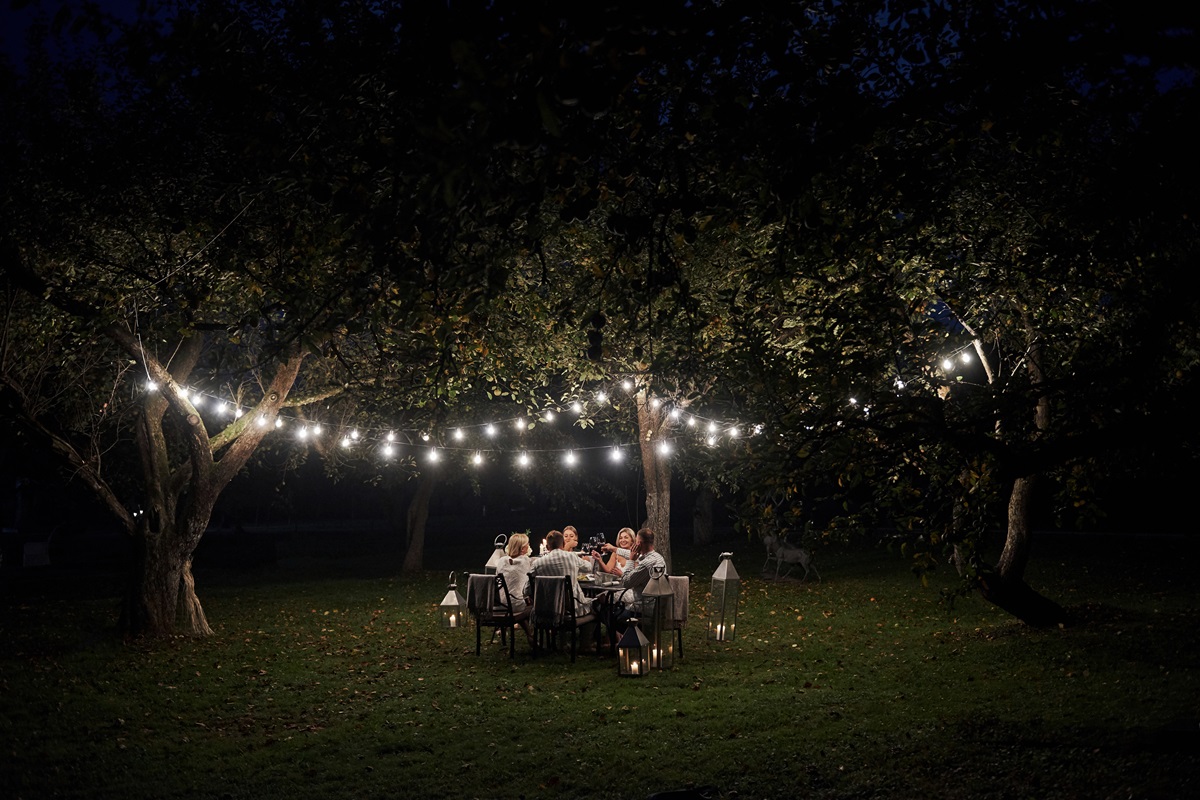 Friends dining under string lights strung between trees in a dark backyard