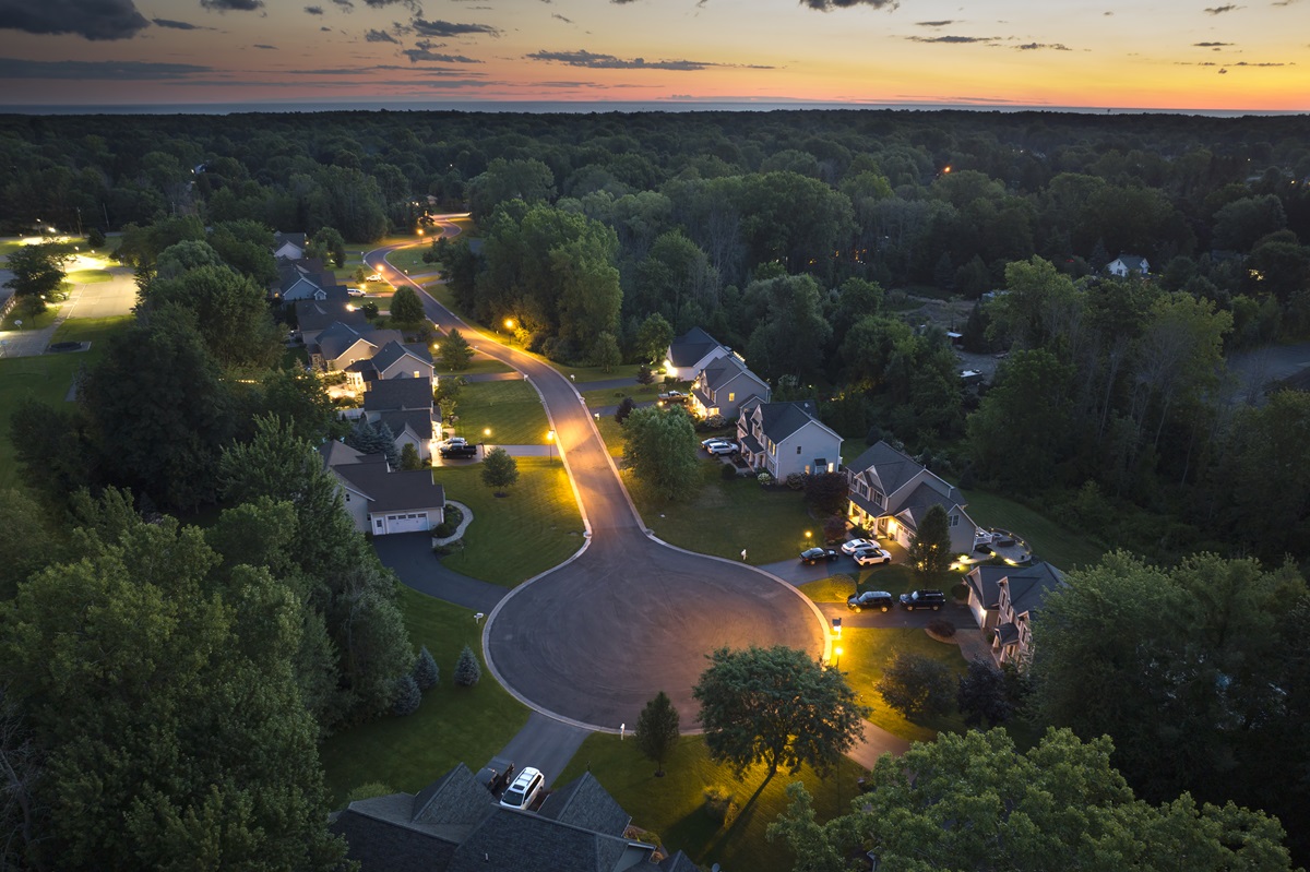 Aerial view of a wooded suburban cul-de-sac lit by street and driveway lights at dusk