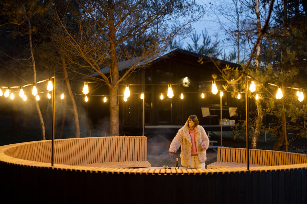 Woman at a round wooden deck lit by hanging bistro string lights at night