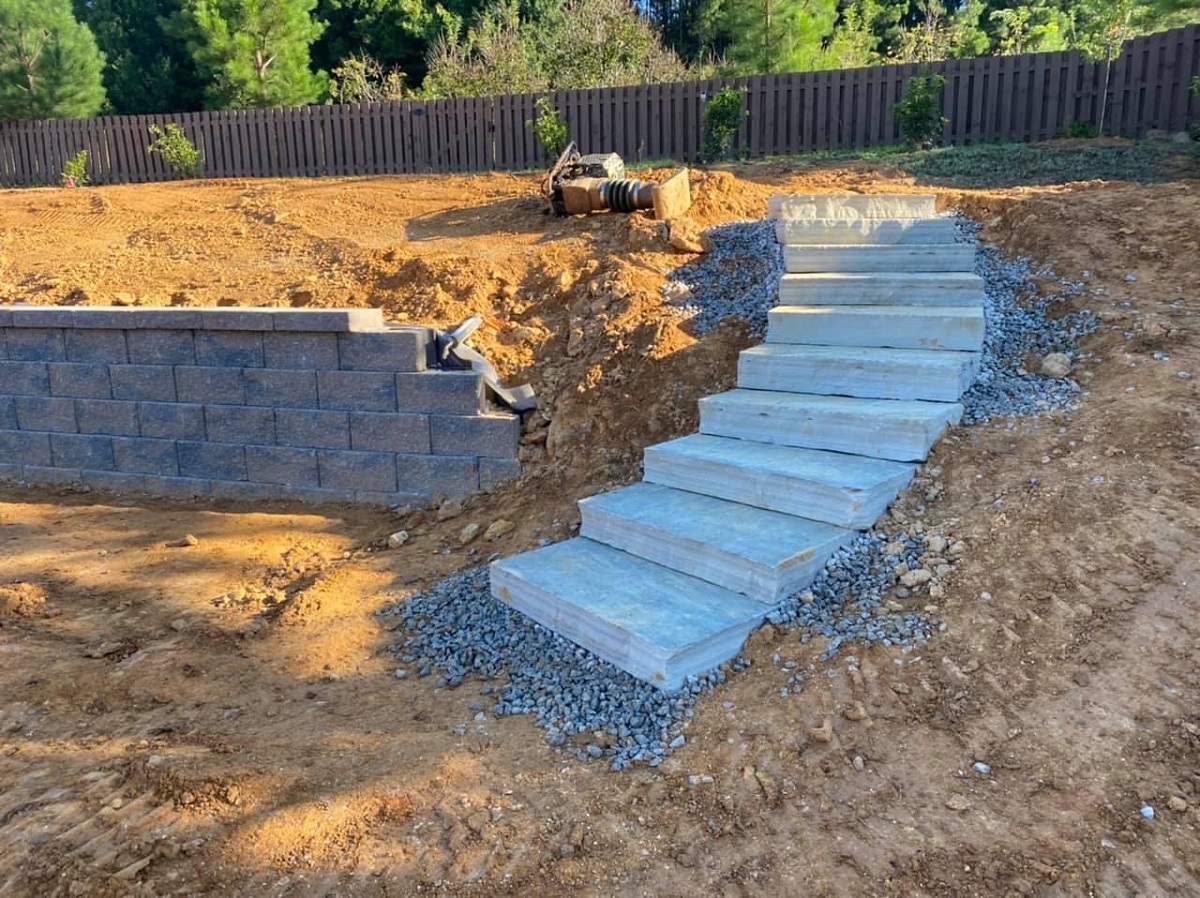 Block retaining wall and stone slab steps under construction on a graded lot