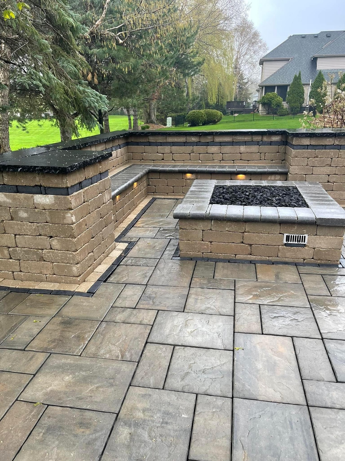 Wet stone patio with a square gas fire pit and an L shaped seat wall with lighting