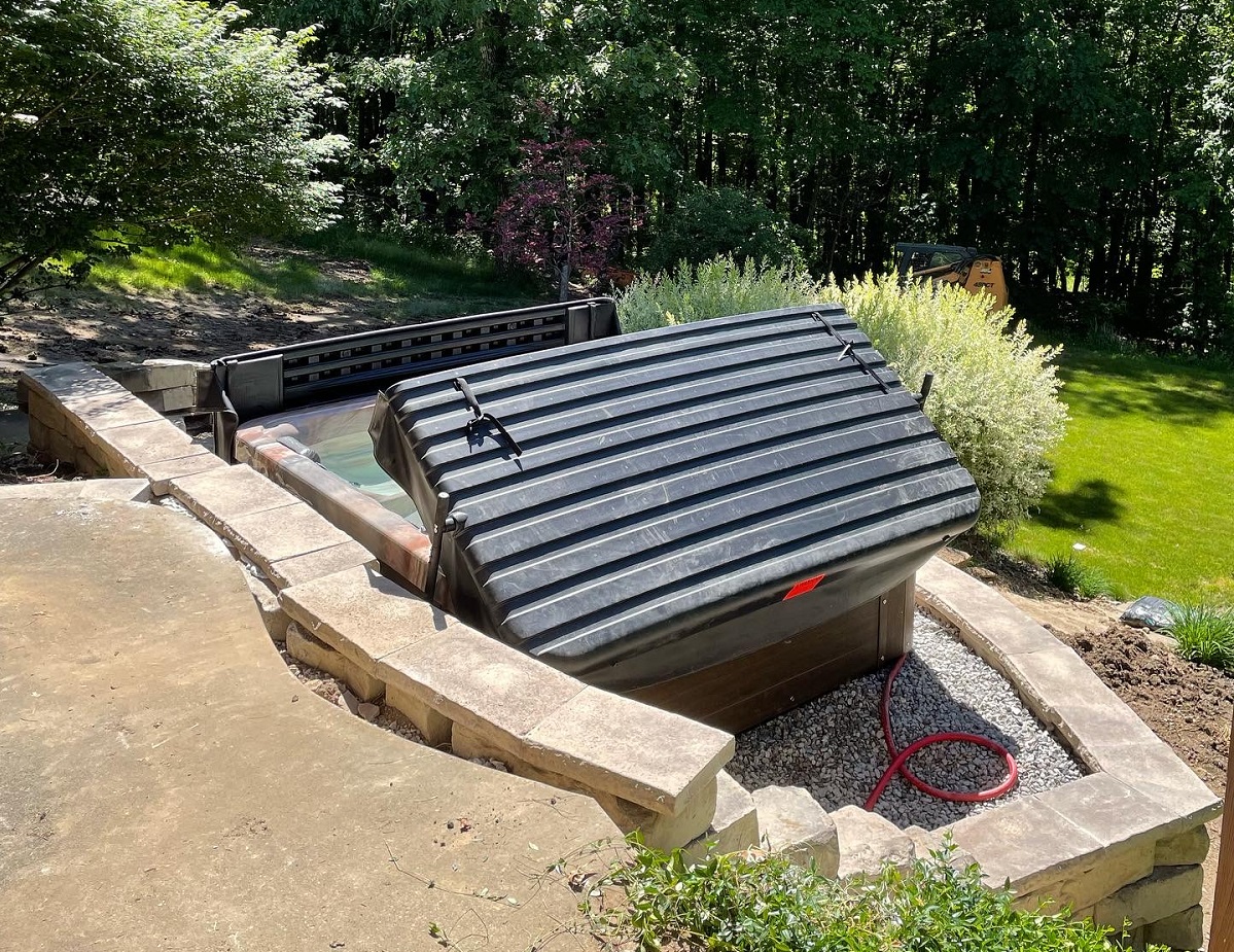 Hot tub set into a stone wall surround with a gravel bed and concrete pad