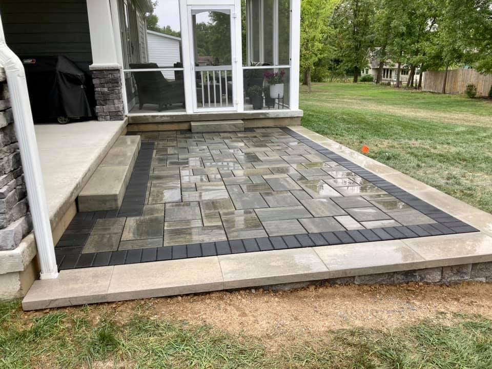 Paver patio with a dark border laid beside a screened porch and lawn