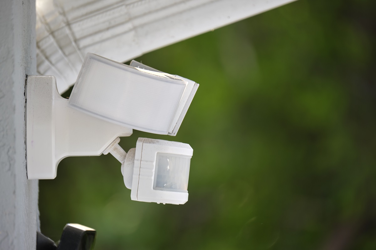 Close-up of a white motion-sensor security floodlight mounted on a house wall