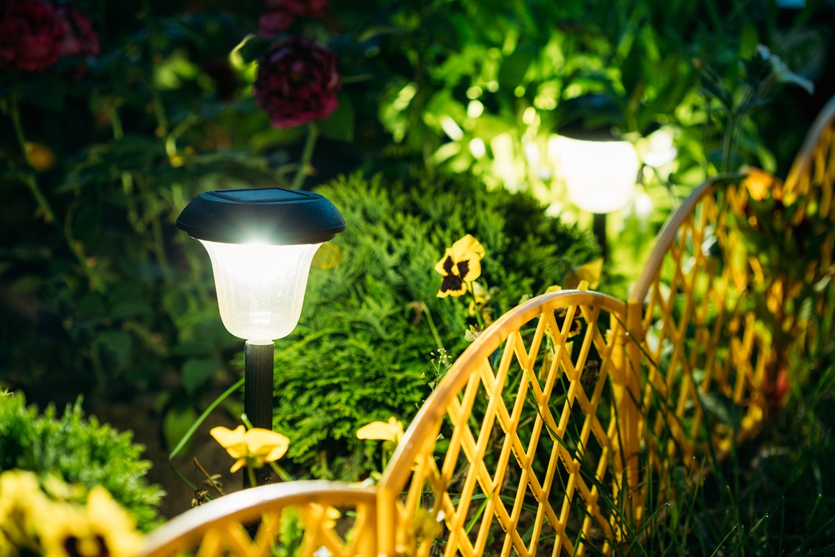 Solar-powered path light glowing beside pansies and a low garden border fence