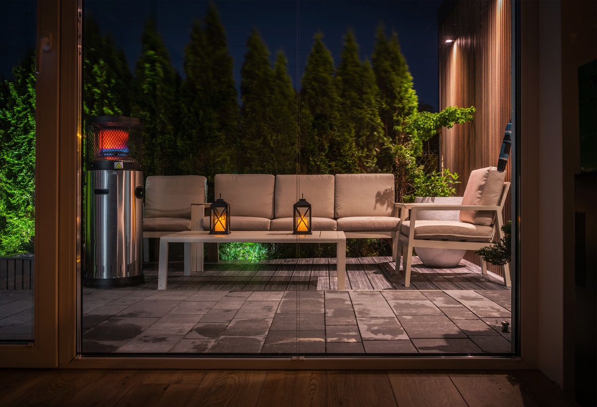 Patio seen through glass doors at night with lanterns, patio heater and lounge seating