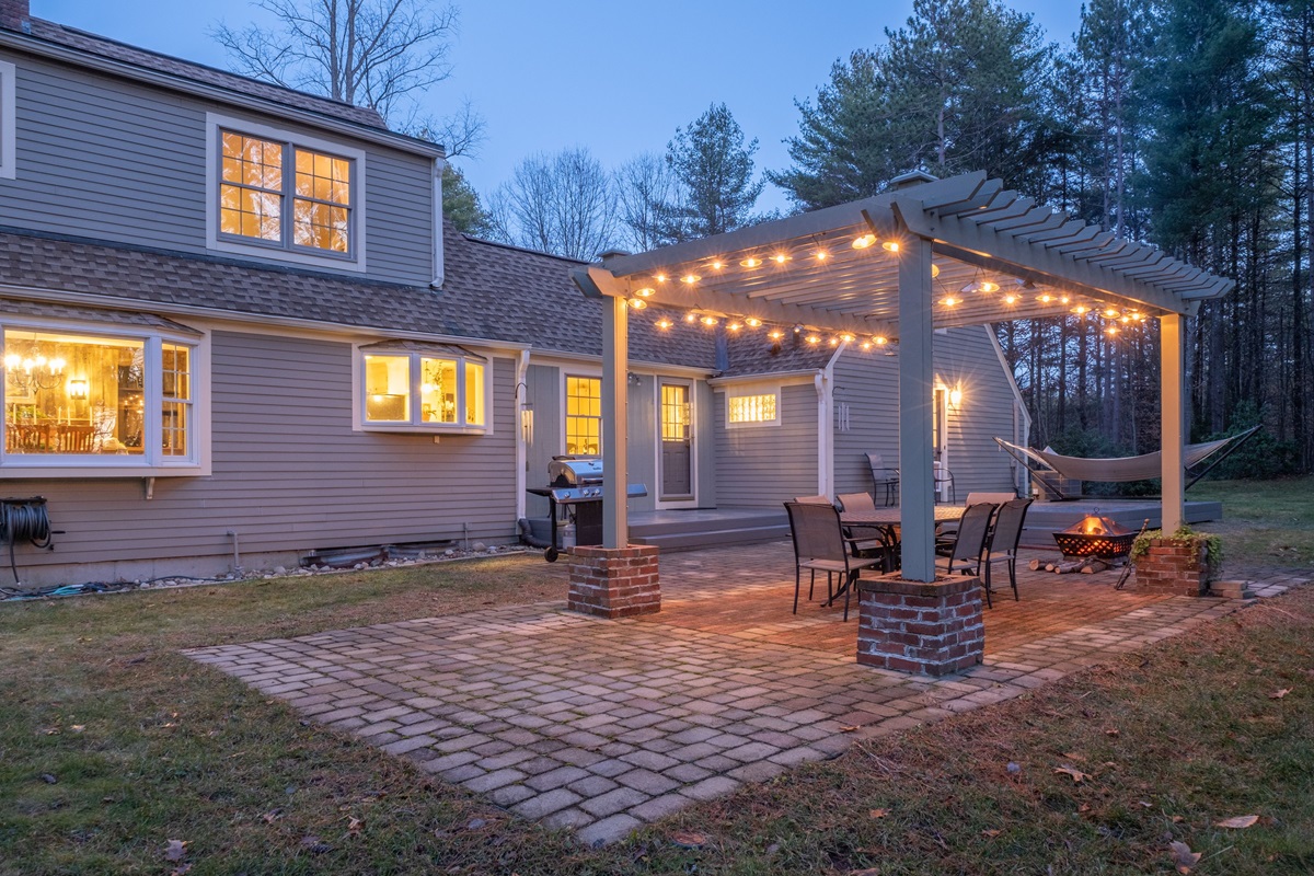 Backyard paver patio with a pergola strung with lights, dining set and fire bowl