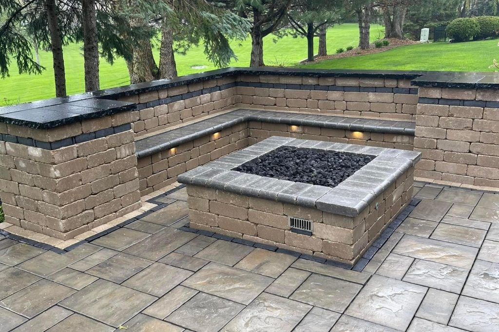 Square gas fire pit set in a paver patio with curved seat walls and built-in wall lighting, built by Daily Landscaping