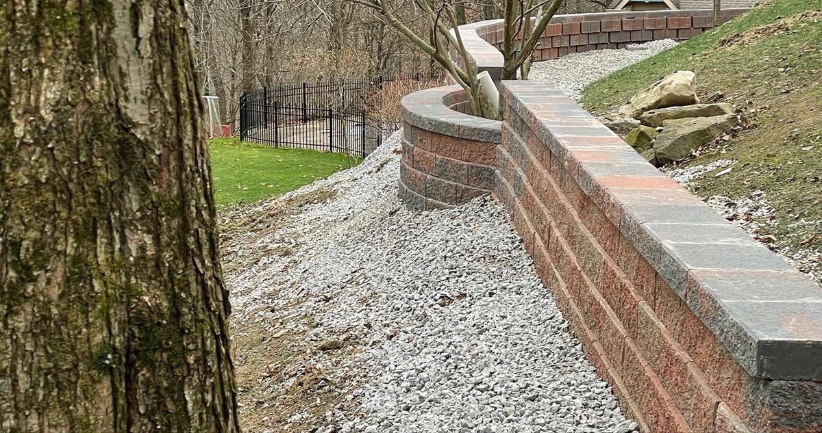 How Retaining Walls Can Improve Drainage and Prevent Erosion in Zelienople Landscapes 5 Long brick retaining wall with a curved planter and gravel drainage strip behind it