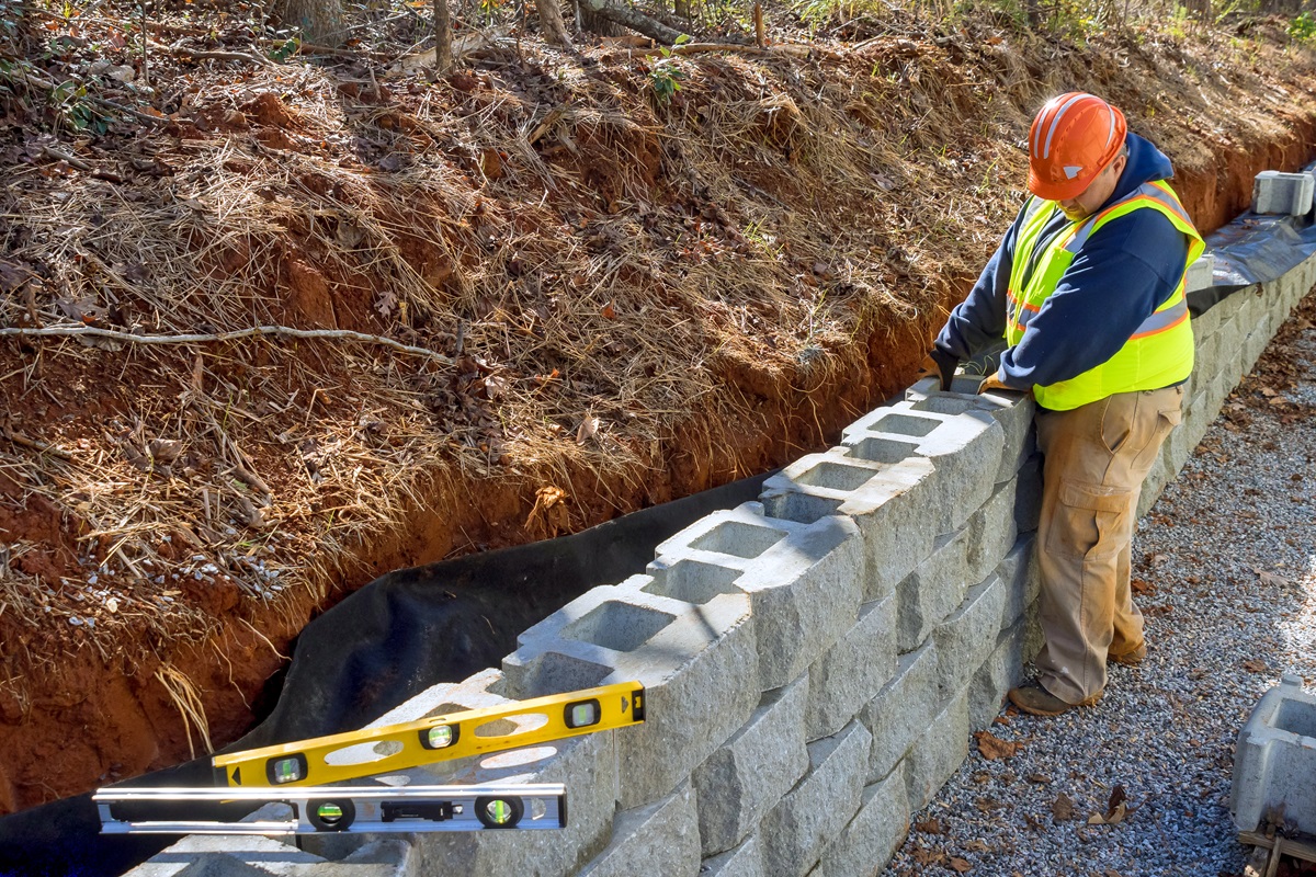 How Retaining Walls Can Improve Drainage and Prevent Erosion in Zelienople Landscapes 4 Worker setting concrete retaining wall blocks with a level above a drainage trench