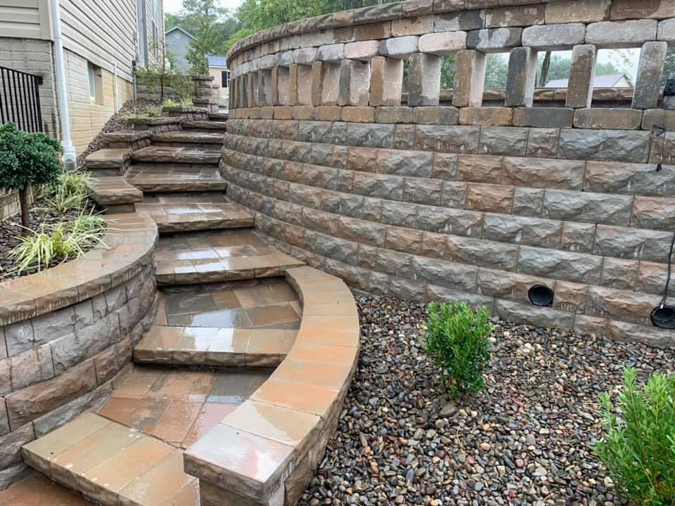 How Retaining Walls Can Improve Drainage and Prevent Erosion in Zelienople Landscapes 1 Curved segmental block retaining wall with paver steps and a river rock drainage bed