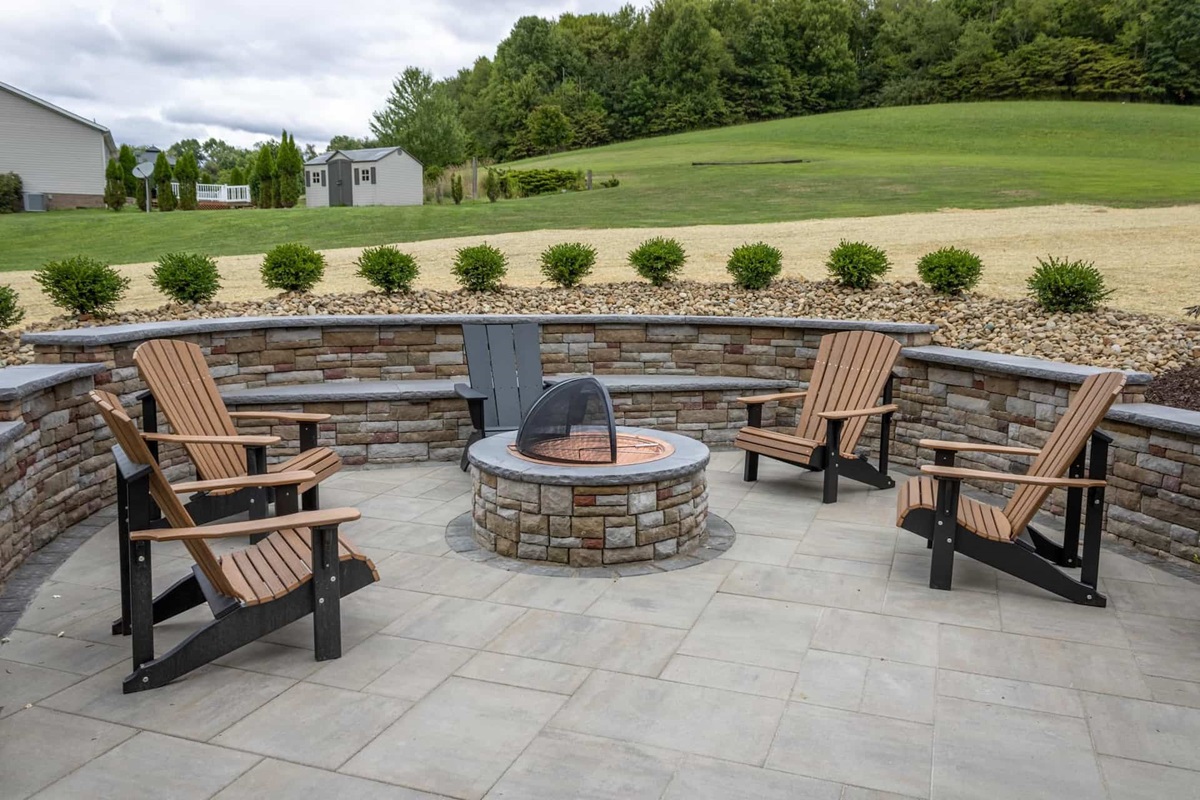 Paver patio with a round stone fire pit, Adirondack chairs and a curved seat wall