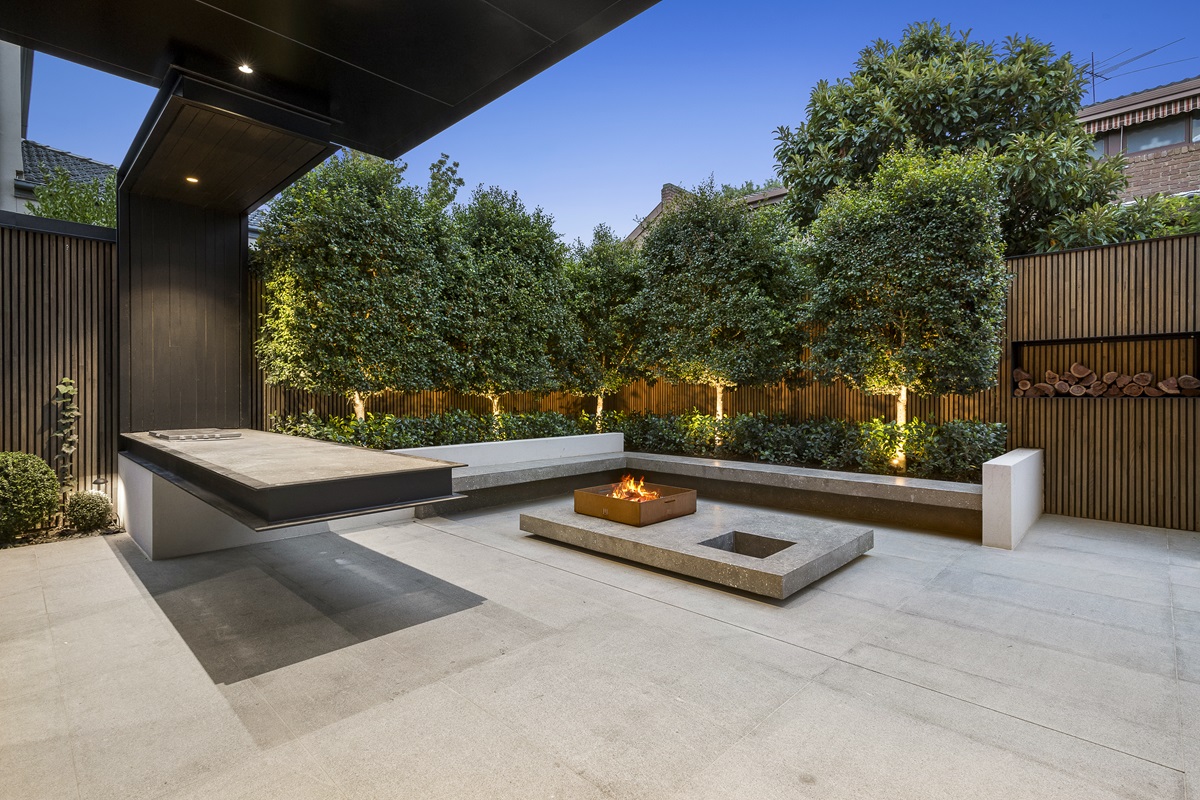 Dark toned courtyard patio with a square fire pit, built in bench and firewood niche
