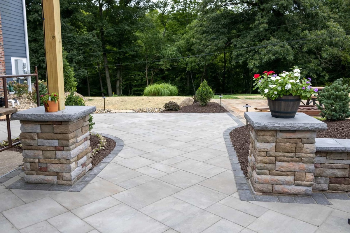 Large paver patio with stone veneer columns, planter urns and mulched shrub beds