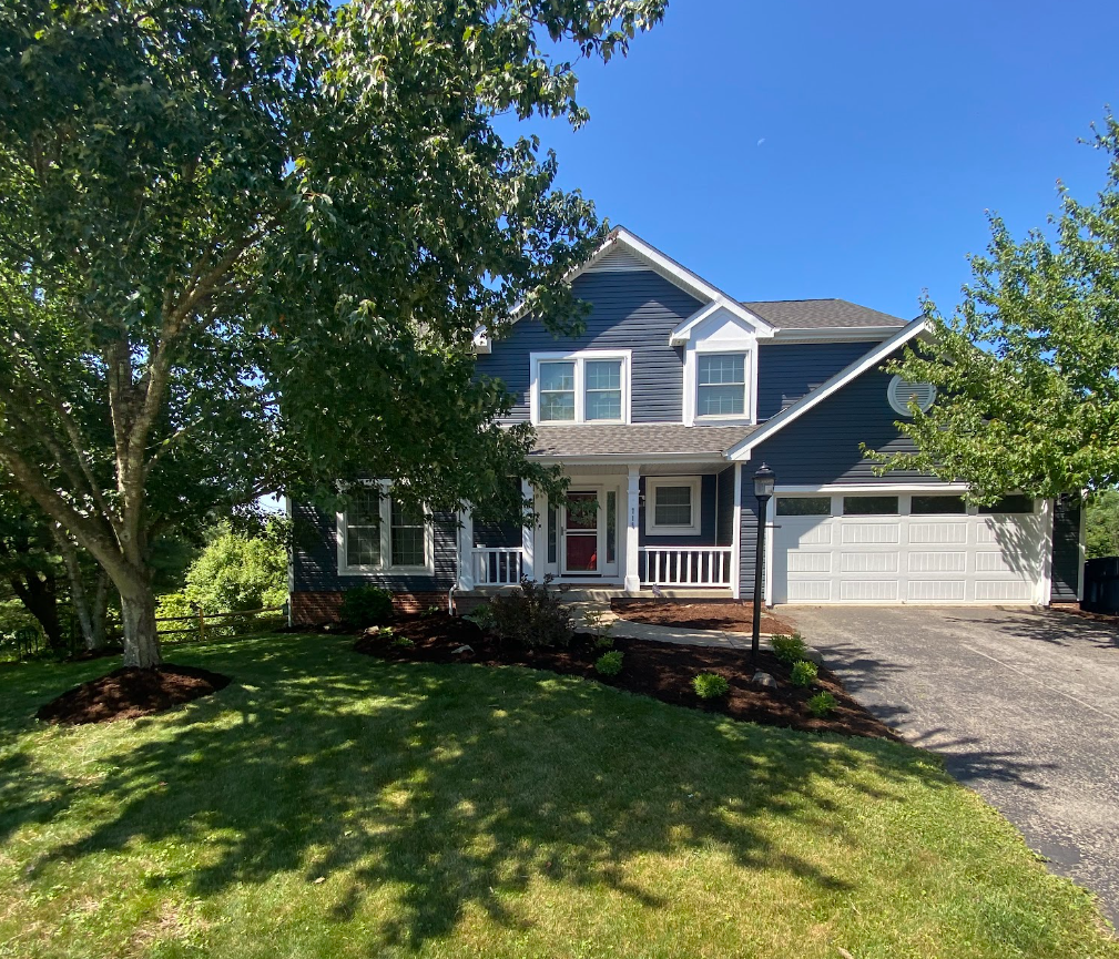 Two story blue house with a front lawn, fresh dark mulch beds and trimmed shrubs