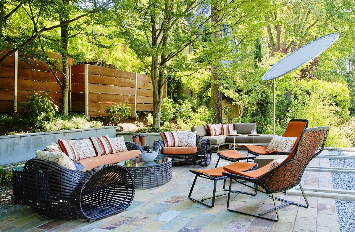 Stone tile patio with woven outdoor furniture, orange cushions and a cedar privacy fence