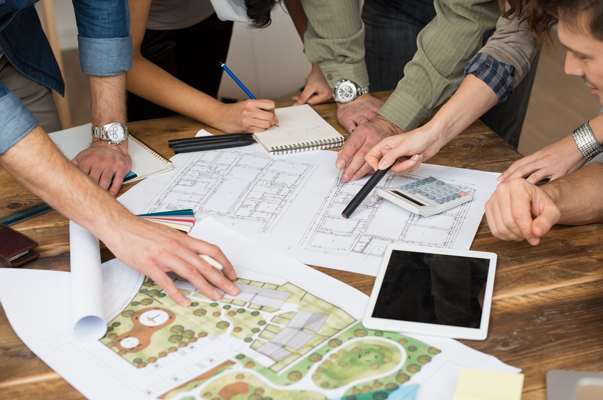 Design team reviewing blueprints and a watercolor landscape site plan on a table