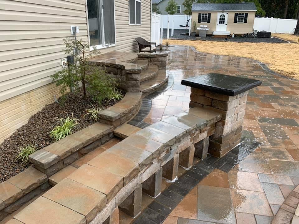 Paver patio with curved seat walls and a stone pillar, wet after rain