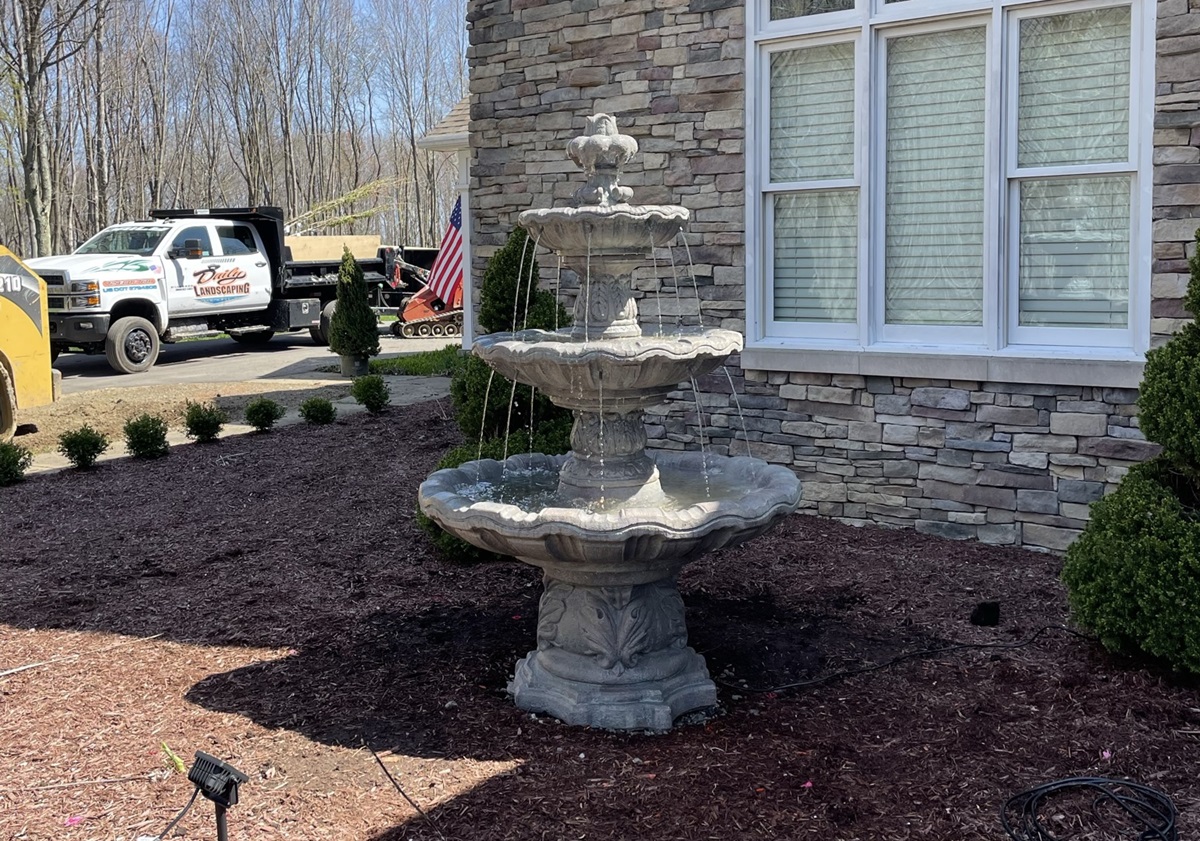 Daily Landscaping truck and skid steer behind a three tier fountain in a fresh mulch bed