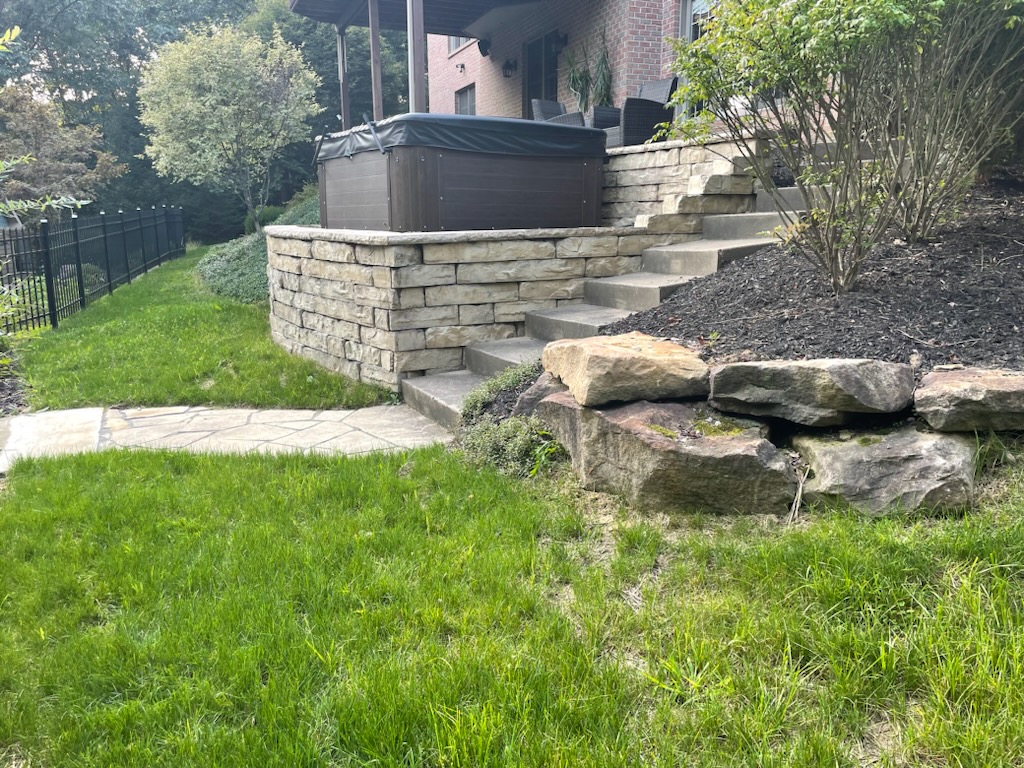 Stone retaining wall holding a hot tub, with stone steps and a flagstone path