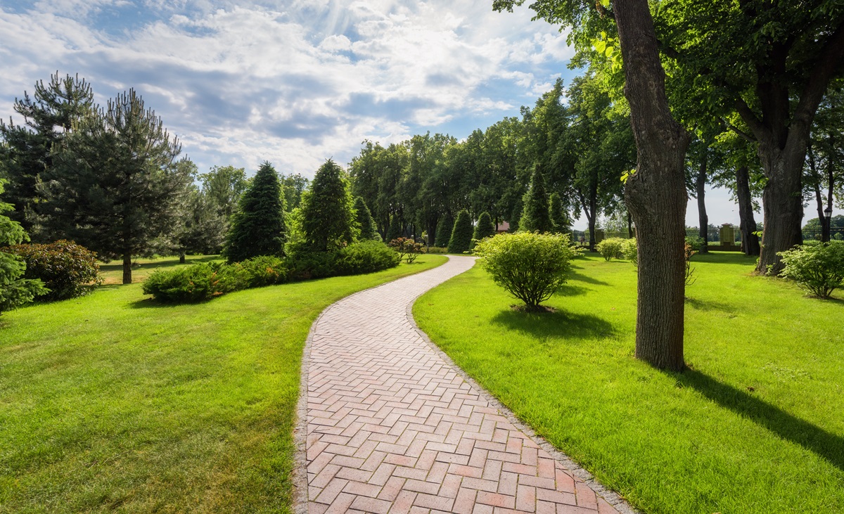 Curving herringbone brick paver walkway through a manicured park lawn