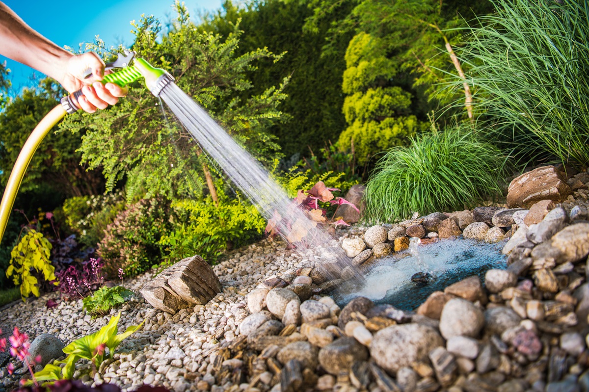 Hand watering a pebble and rock garden bed with a hose spray nozzle