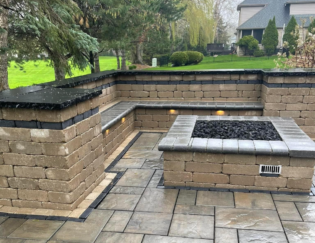 Paver patio with a square gas fire pit and an L shaped seat wall with cap lighting