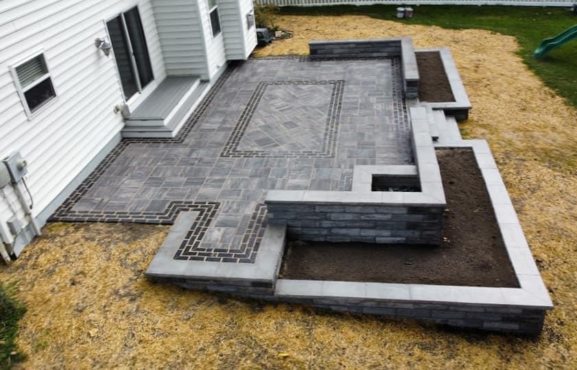 Aerial view of a grey paver patio with a border inlay and raised block planter beds