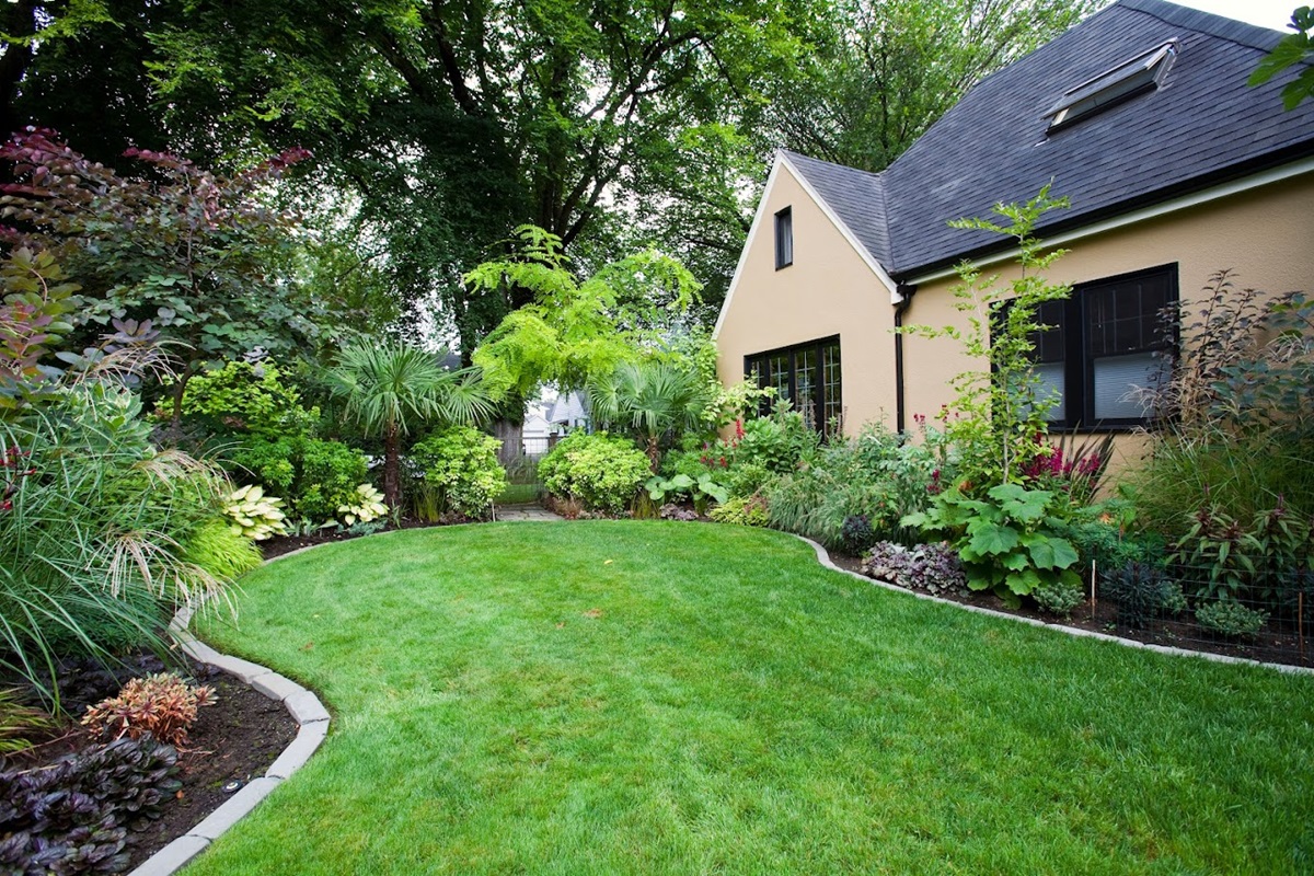 Curved lawn edged with concrete curbing beside layered shrub borders and a stucco house