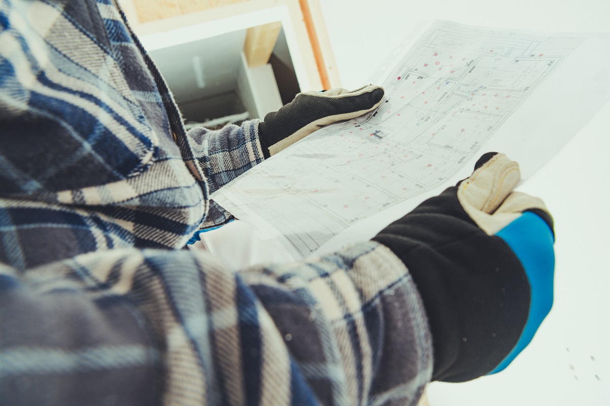 Contractor in a plaid flannel shirt and work gloves reading construction blueprints