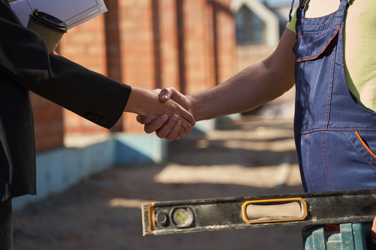 Handshake between a homeowner and a contractor in overalls at a job site