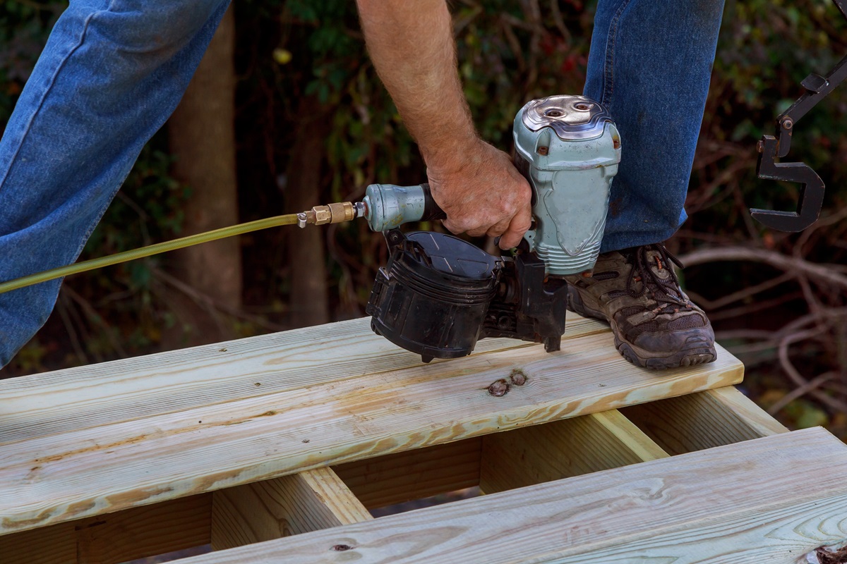 Carpenter using a pneumatic nail gun to fasten pressure treated deck boards to joists