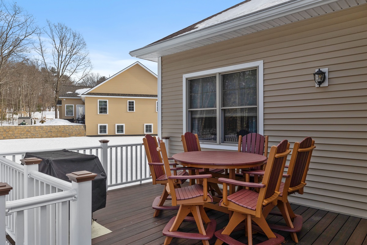 Wood deck with a red patio table, chairs and covered grill beside a snow covered yard