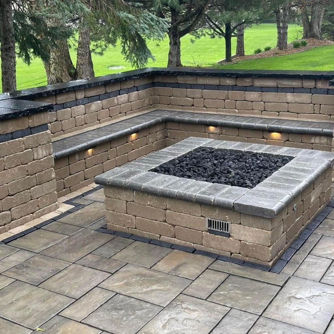 Square gas fire pit set in a paver patio with curved seat walls and built-in wall lighting, built by Daily Landscaping
